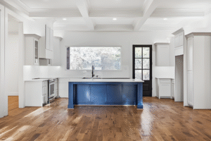 Modern kitchen with white cabinets, a blue island, wood flooring, large window, and glass door. Brightly lit and spacious—ideal for showcasing the craftsmanship of a Dallas custom home builder.