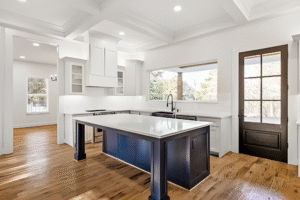 Modern kitchen with white cabinets, a large navy blue island, wood flooring, recessed lighting, and a glass door leading outside—perfectly crafted by a top Dallas custom home builder.