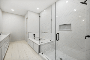 Modern bathroom with a glass-enclosed shower, built-in bathtub, double sink vanity, and white tile flooring, designed by a leading Dallas custom home builder.