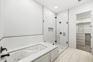 Modern bathroom with a built-in bathtub, glass-enclosed shower, tile flooring, and an adjacent walk-in closet with shelving units—designed by a leading custom home builder in Dallas.