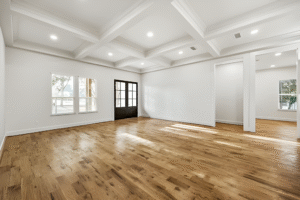 Spacious empty room with light wood floors, white coffered ceiling, recessed lighting, large windows, and double glass doors—perfect inspiration for custom home construction Dallas homeowners desire.