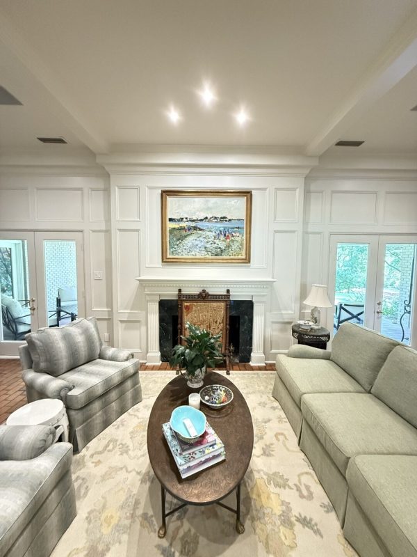 A living room with a light green sofa, armchair, coffee table with books and decor, a fireplace, and a landscape painting above the mantel—expertly crafted by About Custom Coats Remodeling, a leading remodeling company DFW.