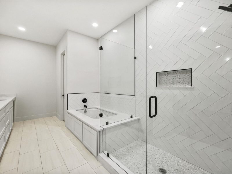 Modern bathroom with a glass-enclosed shower, white herringbone tile walls, built-in bathtub, double sinks, and recessed lighting—perfect inspiration for your next Dallas Bathroom Renovation.
