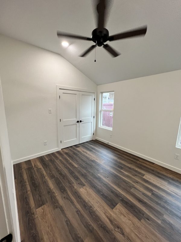 Empty room with white walls, wood-patterned floor, double doors, two windows, and a ceiling fan with lights—ready for your next Dallas Kitchen Renovation or Home Remodeling Dallas TX project.